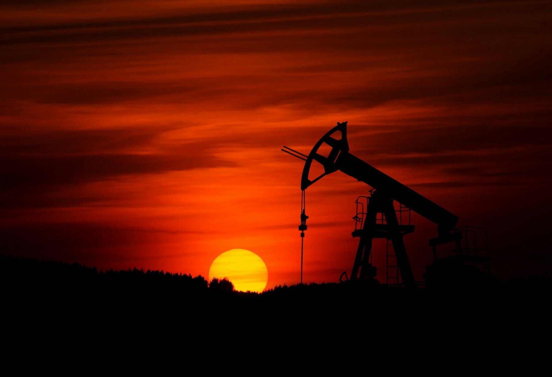 A pumpjack silhouetted against a deep red sunset — oilfield operations at the end of a shift