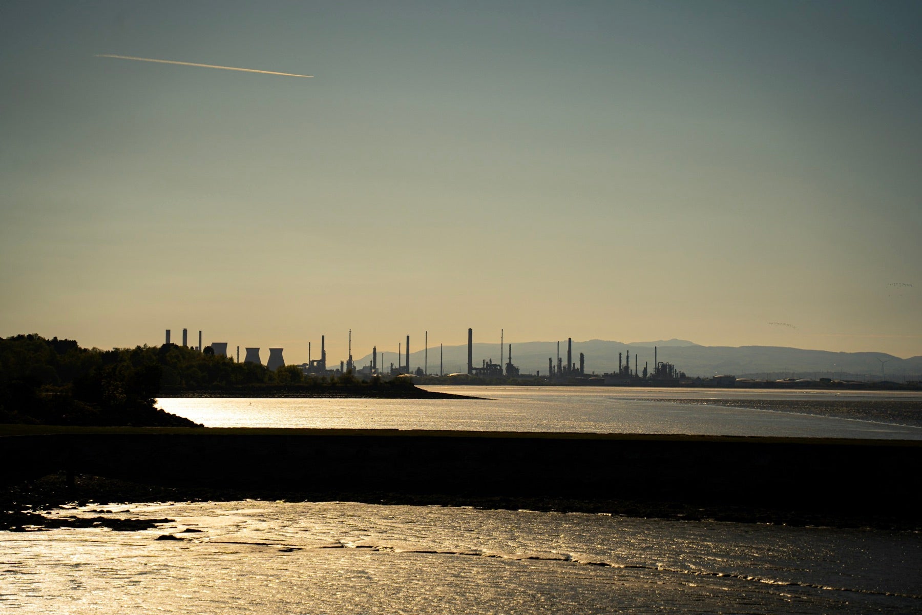 A refinery skyline silhouetted at dusk across a quiet bay